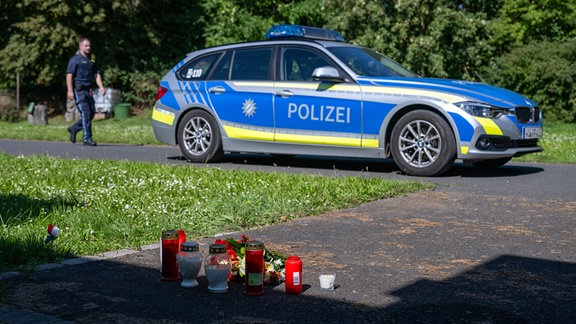 Kerzen und Blumen sind vor einem Seiteneingang des Schulzentrums in Lohr am Main abgelegt, dahinter steht ein Polizeiwagen.