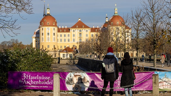 Zwei Frauen stehen vor einem Banner zur Eröffnung der traditionellen Winterausstellung «Drei Haselnüsse für Aschenbrödel» zum gleichnamigen Kultfilm vor Schloss Moritzburg.