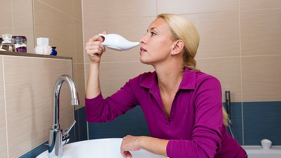 Eine blonde Frau benutzt ein Nasenspuelkaennchen im Badezimmer 