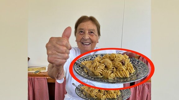 Frau hält Teller mit Pasta in die Kamera und zeigt den Daumen nach oben