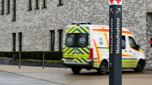 Ein Rettungswagen fährt hinter einem Notaufnahme-Schild in ein Krankenhaus.