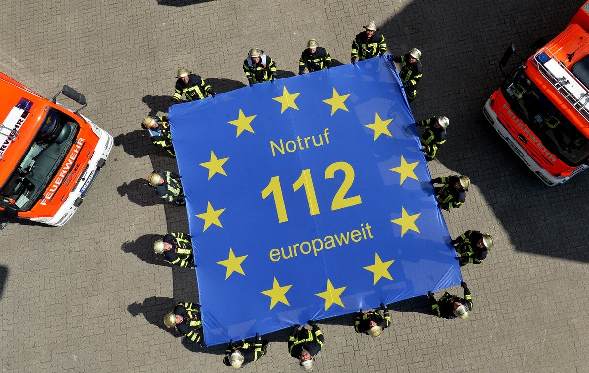 Feuerwehrmänner der Feuerwache 1 in Stuttgart halten eine Fahne mit der Aufschrift «Notruf 112 europaweit»