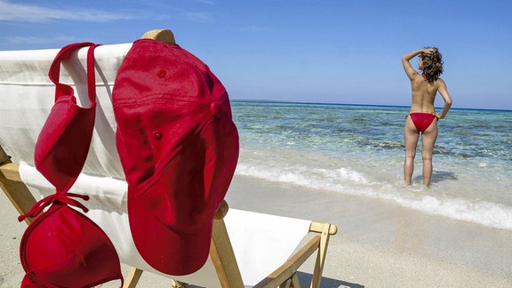 Liegestuhl am Strand, Frau steht am Wasser