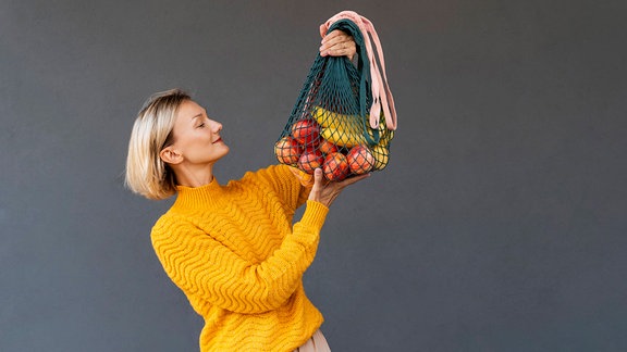 Frau schaut lächelnd auf Obst in einem Einkaufsnetz.