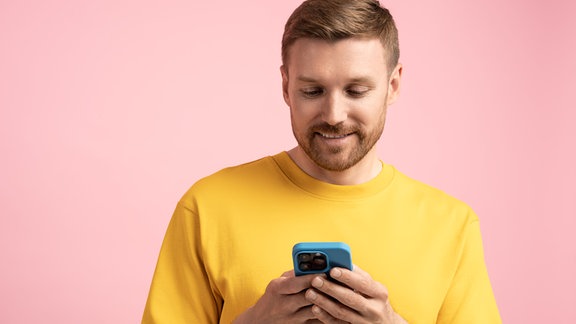 Symbolfoto: ein lächelnder, junger Mann an einem Smartphone.