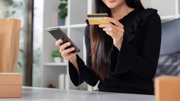 Eine Frau die mit Kreditkarte und Smartphone einen Online-Einkauf tätigt.