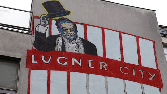 An einer Hausfassade ist ein Wandgemälde auf dem Lugner City steht.