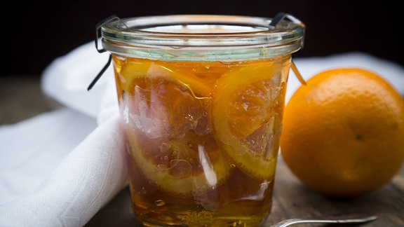 Ein Glas Orangenmarmelade, umgeben von Serviette, Orange und Löffel
