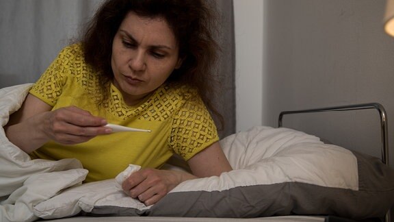 Eine Frau liegt mit Fieberthermometer im Bett.