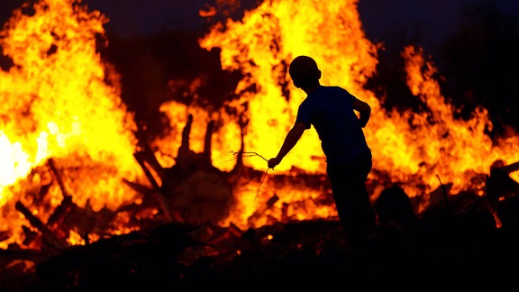 Ein Kind wirft Äste in ein großes Osterfeuer