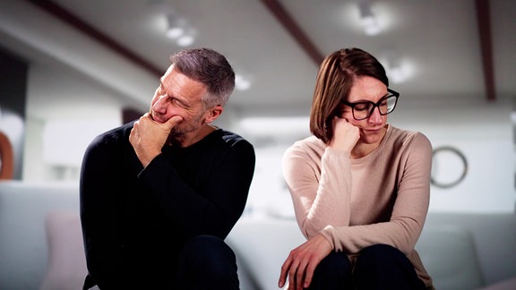 Ein Mann und eine Frau sitzen nebeneinander und schauen in die jeweils andere Richtung