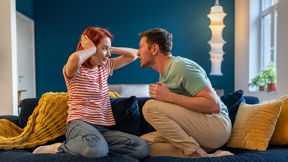Ehemann schreit seine Frau an, die zu Hause auf der Couch sitzt