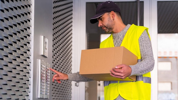 Ein Zusteller mit einem Paket klingelt an einer Haustür