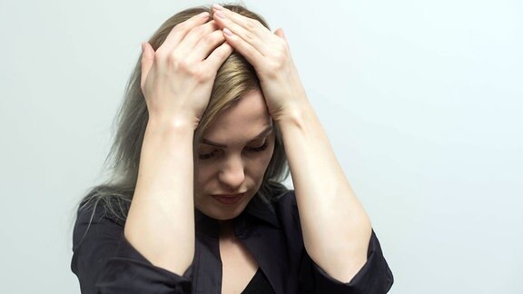 Traurige, müde junge Frau, die die Stirn berührt und unter Kopfschmerzen, Migräne oder Depressionen leidet.