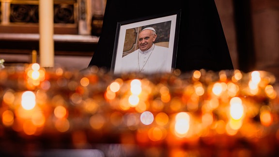 Ein Bild des verstorbenen Papst Franziskus ist im Freiburger Münster hinter einigen brennenden Kerzen zu sehen.