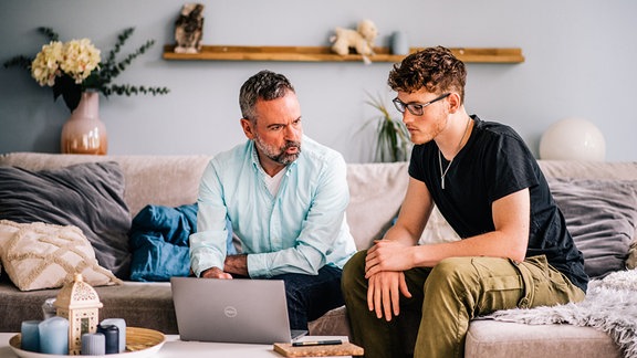 Ein Vater sitzt mit seinem Sohn an einem Laptop.