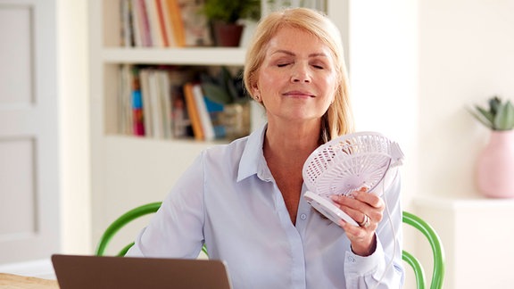 Eine Frau in den mittleren Jahren führt sich Luft mit einem Ventilator zu.