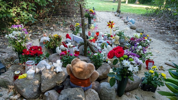 Nahe der Stelle in Pragsdorf, wo ein Sechsjähriger am 14.09.2023 mit Stichverletzungen gefunden wurde, an denen er später verstarb, steht ein buntes Kreuz und liegen Plüschtiere znn Blumen.