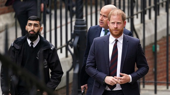 Prinz Harry (r) wird von Sicherheitskräften eskortiert, als er am Royal Courts of Justice eintrifft.