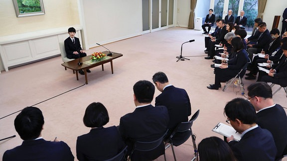 Prinz Hisahito von Japan sitzt an einem Tisch vor einem Publikum.