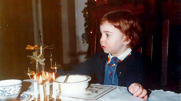 Ein Kind sitzt an einem Tisch und betrachtet die Kerzen einer Weihnachtspyramide.