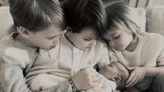 Drei Kinder halten ein Baby.