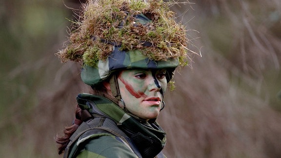 Prinzessin Victoria trägt Militärkleidung und einen Helm mit Moos drauf.