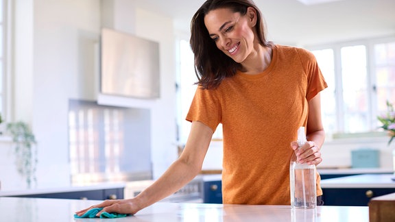 Symbolbild: Frau wischt lächelnd eine Küchen-Arbeitsfläche