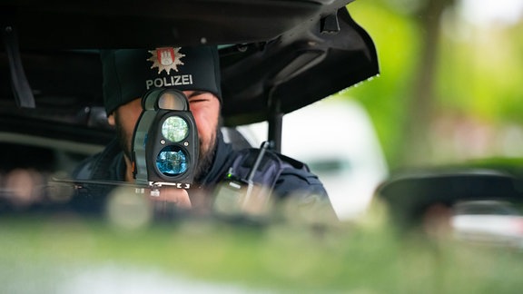 Ein Polizist kontrolliert mit einem Messgerät die Geschwindigkeit von Fahrzeugen in einer 30er-Zone.
