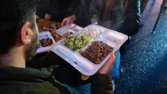 Menschen geben sich während des 5. Fastenbrechens der "Initiative gemeinsames Fastenbrechen" im Bahnhofsviertel Essen weiter.