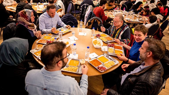 Mitglieder der Gemeinde treffen sich 2023 nach dem Beginn des Fastenmonats Ramadan in der Sehitlik-Moschee zum ersten Iftar, dem Fastenbrechen, und sitzen beim Essen zusammen.