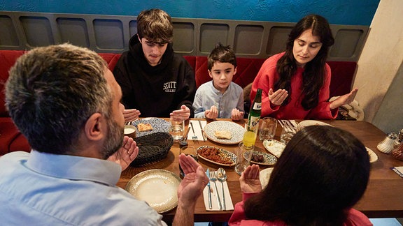 Muslimische Familie beim Tischgebet während des Fastenbrechens in einem Restaurant.