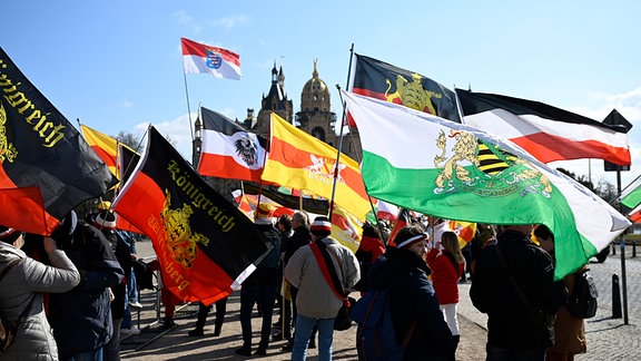 Teilnehmer einer Versammlung von sogenannten Reichsbürgern halten Fahnen in der Hand. 