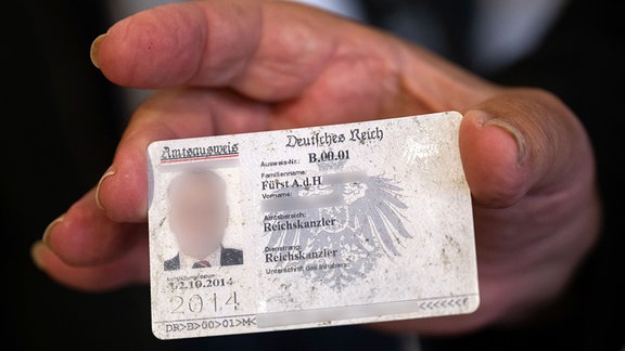 Ein Mann, der sich selbst als «Reichskanzler» bezeichnet, hält seinen selbst erstellten Ausweis in die Kamera.