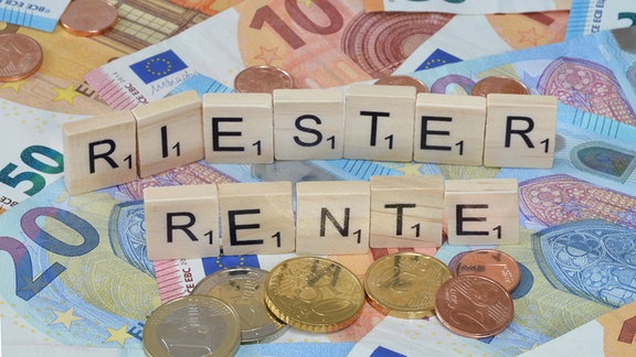 Symbolfoto: Buchstabensteine bilden ein Wort: "Riester Rente", umgeben von Bargeld.