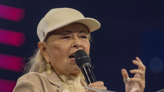 Roseanne Barr hält ein Mikrofon in der Hand.