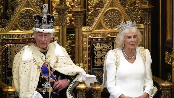 König Charles III. blickt auf, während er darauf wartet, die Rede des Königs zu verlesen, als Königin Camilla bei der Eröffnung des Parlaments im House of Lords neben ihm Platz nimmt.