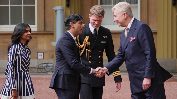 Sir Clive Alderton, Erster Privatsekretär des Königs und der Königin (rechts), und Commander William Thornton, Königliche Marine, Ausbilder des Königs (2. von rechts), begrüßen Großbritanniens bisherigen Regierungschef Rishi Sunak (2.v.l.) und seine Frau Akshata Murty