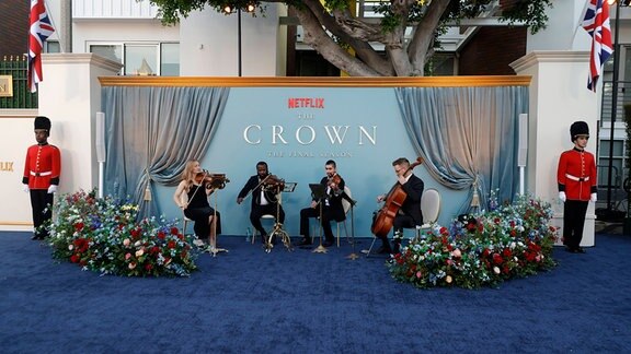 Musiker spielen vor einer Pro,otiontafel mit der Aufschrift "The Crown".