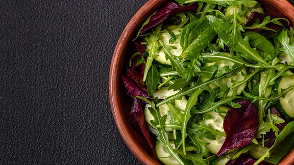 östlicher frischer Salat mit Rucola, Spinat, Gurke und Kirschtomaten auf einem Teller.