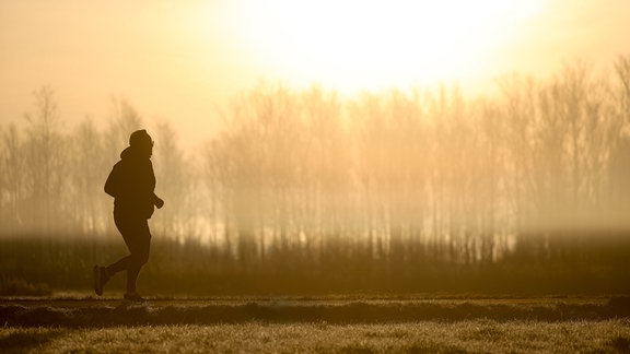 Ein Jogger ist am Morgen im Gegenlicht der Sonne unterwegs, während sich der Himmel durch Saharastaub gelb verfärbt hat.