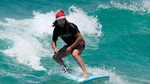 Ein Mann reitet auf einem Surfbrett und trägt eine Weihnachtsmannmütze, während er Weihnachten am Bondi Beach in Sydney feiert. 