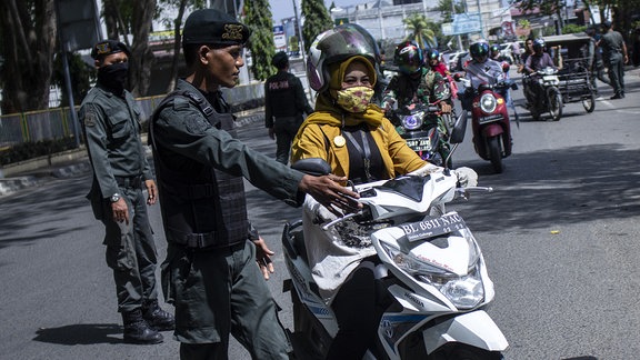 Islamische Sharia-Polizisten halten eine Mopedfahrerin auf, die nicht nach den Regeln der Scharia gekleidet ist.