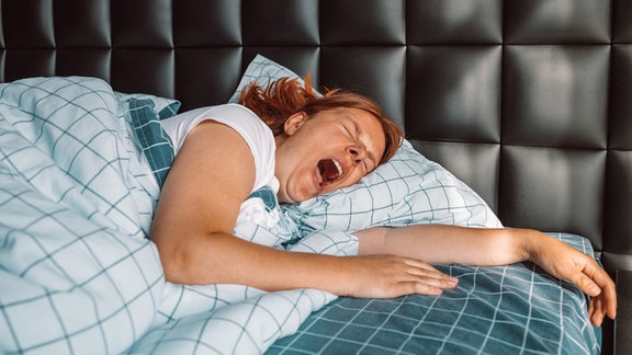 Gähnende Frau, im Bett liegened