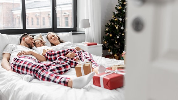 Eine Familie liegt mit Geschenken im Bette