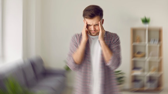 Mann hält sich den Kopf, Umgebung verschwommen