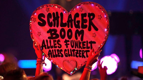 Schild in Herzform mit der Aufschrift Schlager Boom Schlagerbooom 2021 Alles funkelt! Alles glitzert!