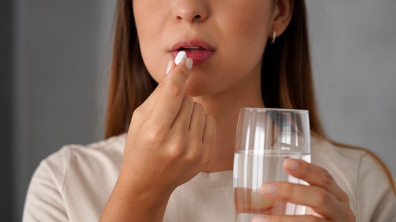 Junge Frau nimmt eine Pille, während sie ein Glas Wasser in der Hand hält