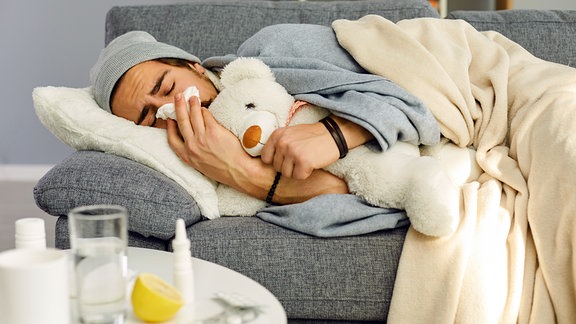 Jung Mann, unter einer Erkältung leidend, liegt auf duf der Couch.