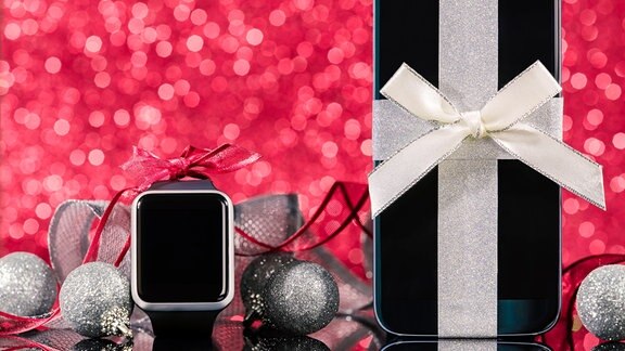 Smartwatch und Smartphone mit Schleifen zwischen Weihnachtskugeln